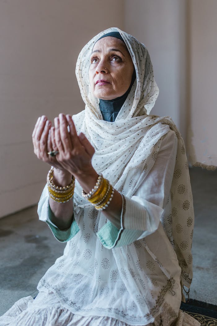 services-01 Senior woman in traditional attire praying indoors, embodying faith and devotion.