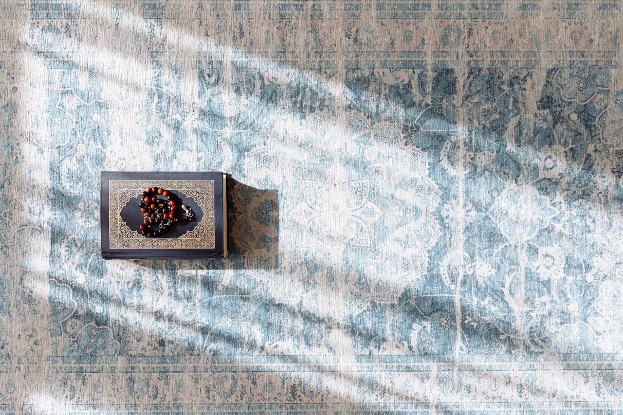 services-03 Quran with prayer beads on a prayer rug bathed in gentle sunlight, evoking spirituality.