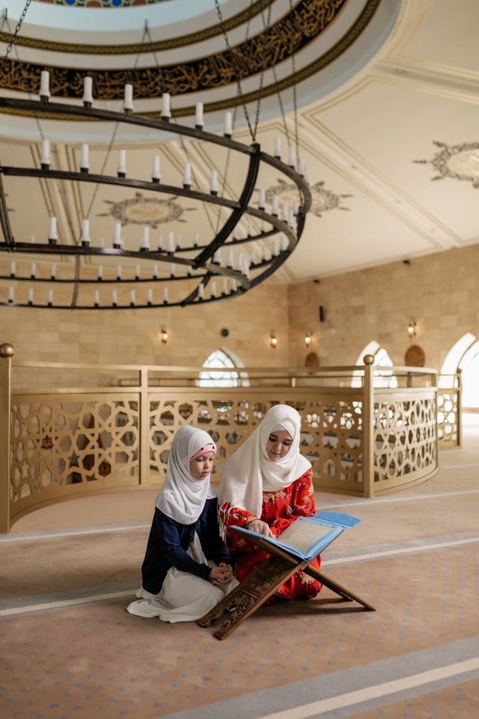 A woman and young girl in hijabs read a Quran together inside a mosque.